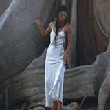 Draped elegantly in a white Peace Silk simple wedding dress from AYA Sacred Wear, a woman stands gracefully on the expansive roots of a gigantic tree. Her boho dress, with its natural silk fabric, harmonizes beautifully with the textures of the bark and roots surrounding her. The scene exudes a tranquil and earthy ambiance.