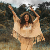 Wearing a Boho Top from AYA Sacred Wear, a woman with curly hair stands in a field, effortlessly draped in the hand-loomed cotton blouse. With her arms raised and surrounded by trees beneath an overcast sky, she embodies a serene and natural atmosphere.