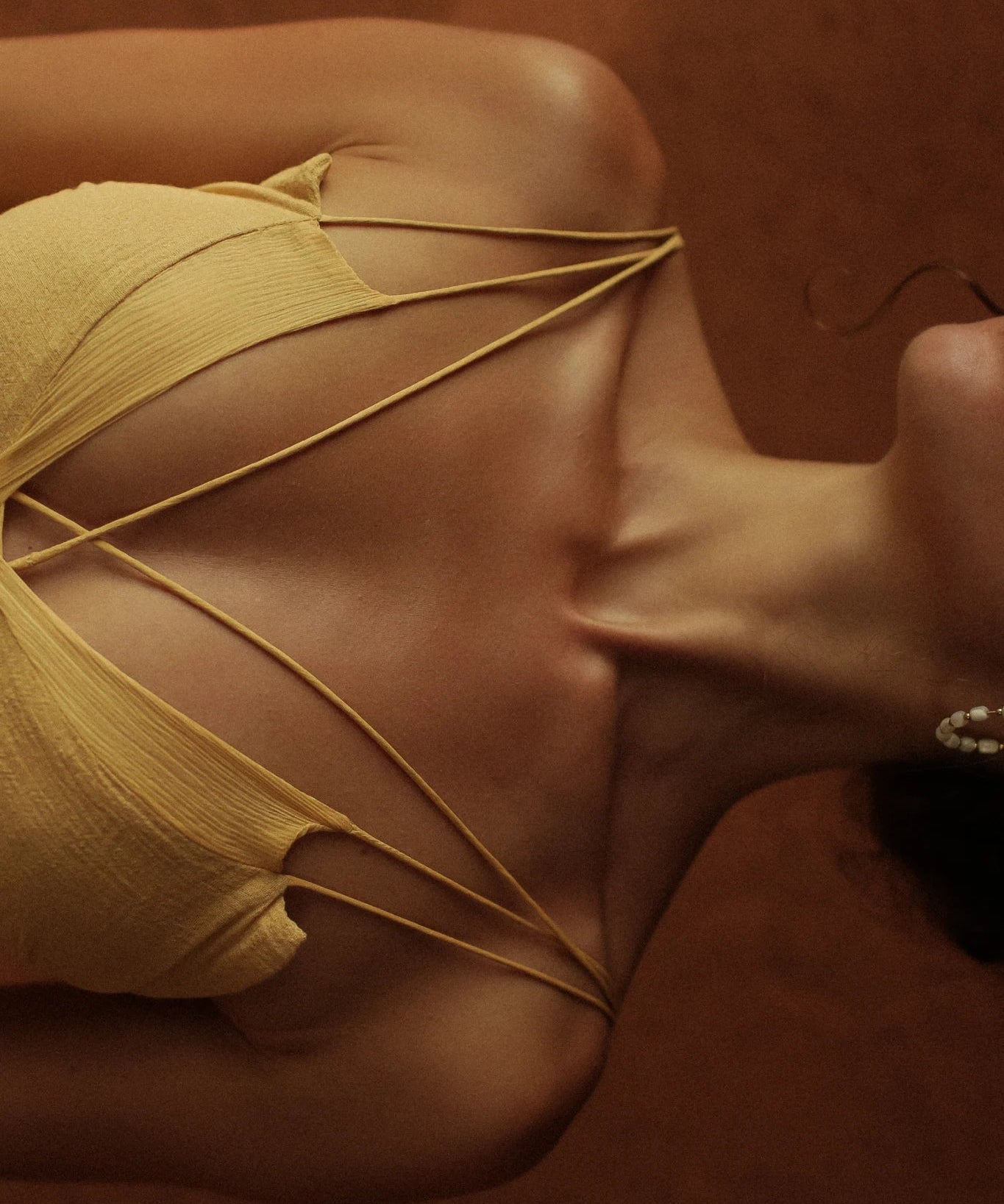 A person wears the AYA Sacred Wear Powder Yellow Padma Dress, shown from the shoulders up with their collarbone and neck visible against a brown background.
