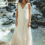 Standing on a rock by a flowing stream, the individual dons the See Through Dress, a long maxi dress with exquisite handmade embroidery by AYA Sacred Wear. The lush greenery enhances the serene beauty of this tribal raw cotton cover-up.