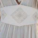 A close-up of the AYA Sacred Wear Tatva Dress Ivory Colour – Sustainable Bohemian Dress highlights its white botanically dyed fabric, wide handcrafted belt with pearl-beaded diamond motifs, and tasseled V-neck tie.